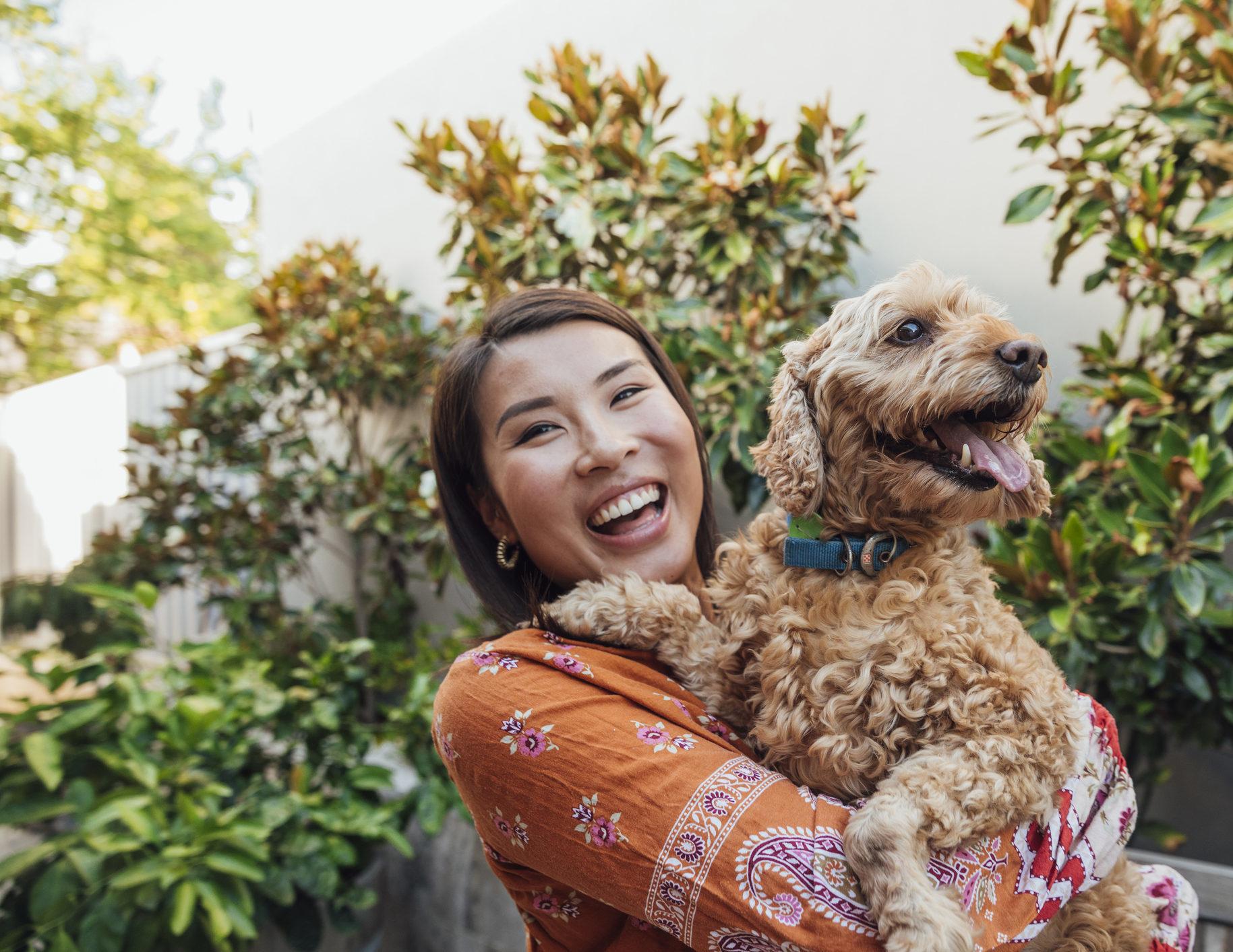 A shot of a young, Asian woman smiling at the camera with her dog.