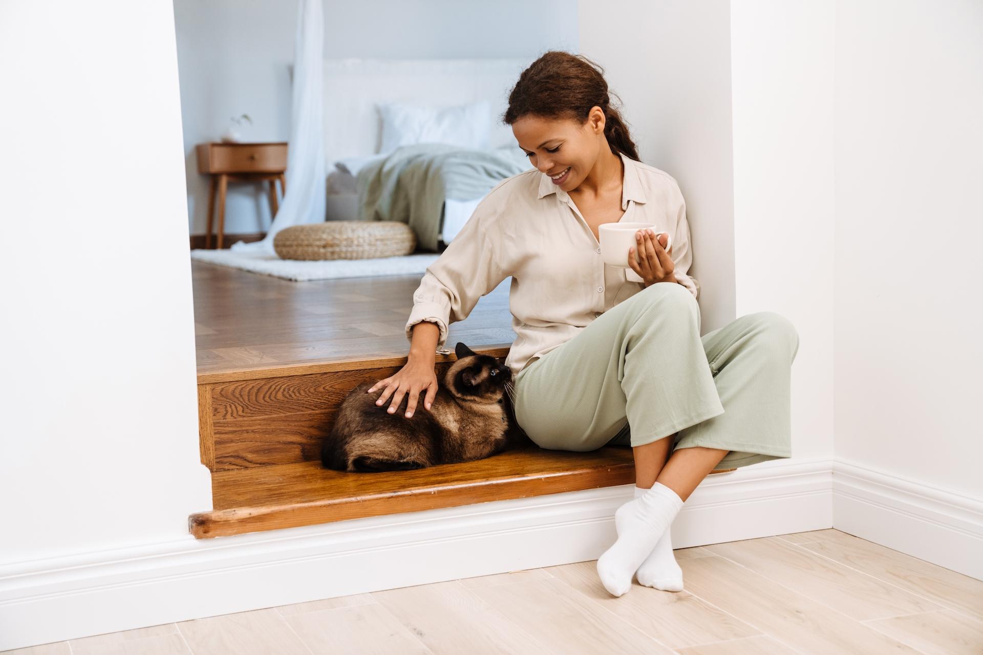 Black woman smiling and petting her cat while sitting on stairs at home